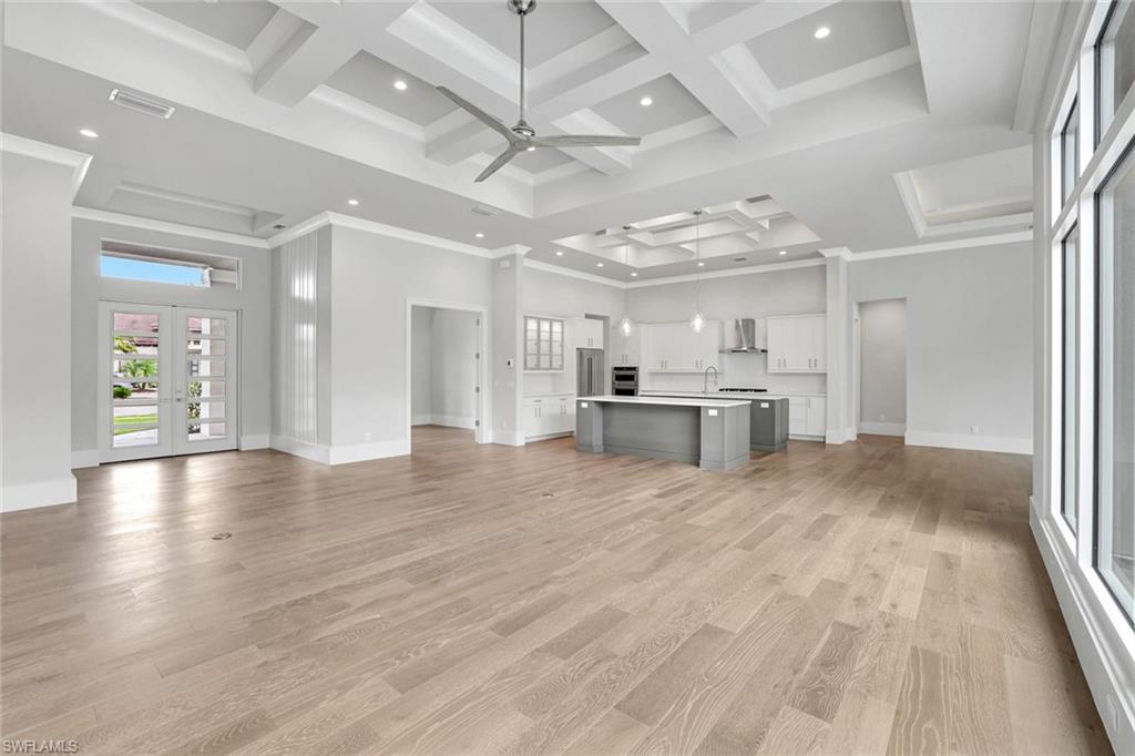 14286 Charthouse Circle Naples, FL 34114 - Photo 7 of 47 Unfurnished living room with french doors, coffered ceiling, a towering ceiling, light wood-style flooring, and a ceiling fan