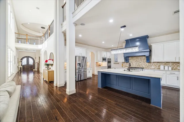 a kitchen with stainless steel appliances granite countertop a refrigerator a sink dishwasher a stove and white cabinets with wooden floor