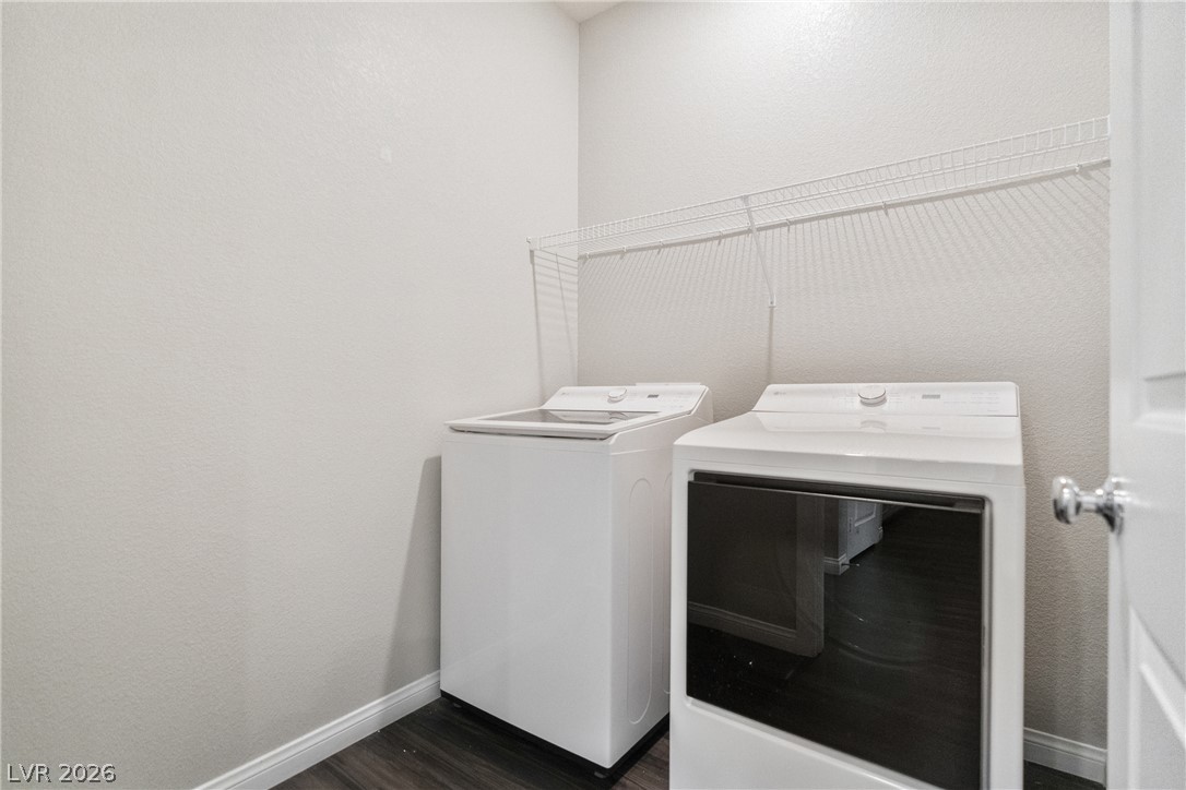 Functional laundry space featuring modern appliances and a wire storage shelf over dark wood flooring.