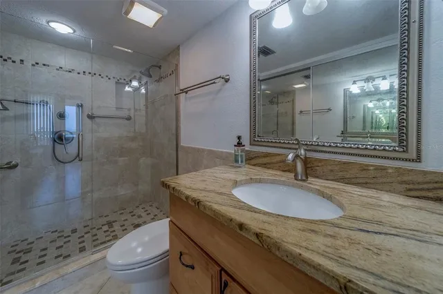 a bathroom with a granite countertop sink a toilet a mirror and shower