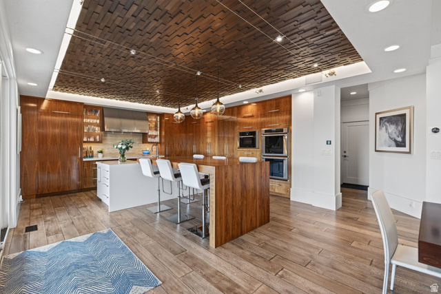12308 Mariah Circle Draper, UT 84020 - Photo 38 of 293 Modern kitchen featuring a textured walnut wood ceiling with recessed lighting, an expansive wood-finish island, integrated stainless steel double ovens, and sleek wood-panel cabinetry