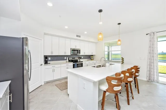 a kitchen with stainless steel appliances kitchen island granite countertop a stove a sink a refrigerator and white cabinets with wooden floor