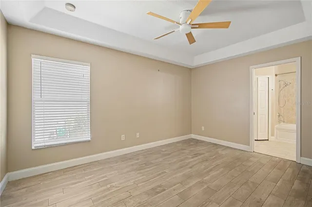 an empty room with wooden floor ceiling fan and windows