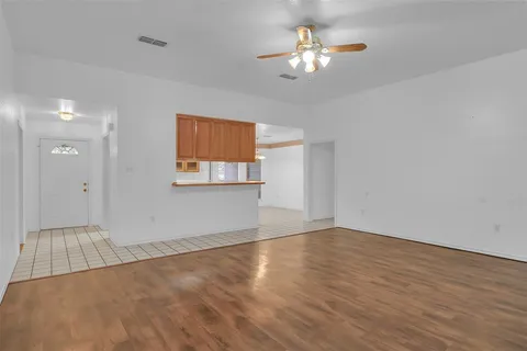 an empty room with wooden floor chandelier fan and windows