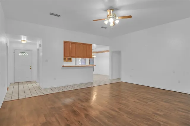 an empty room with wooden floor chandelier fan and windows