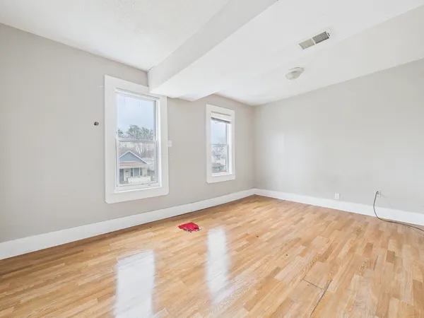 a view of an empty room with wooden floor and a window