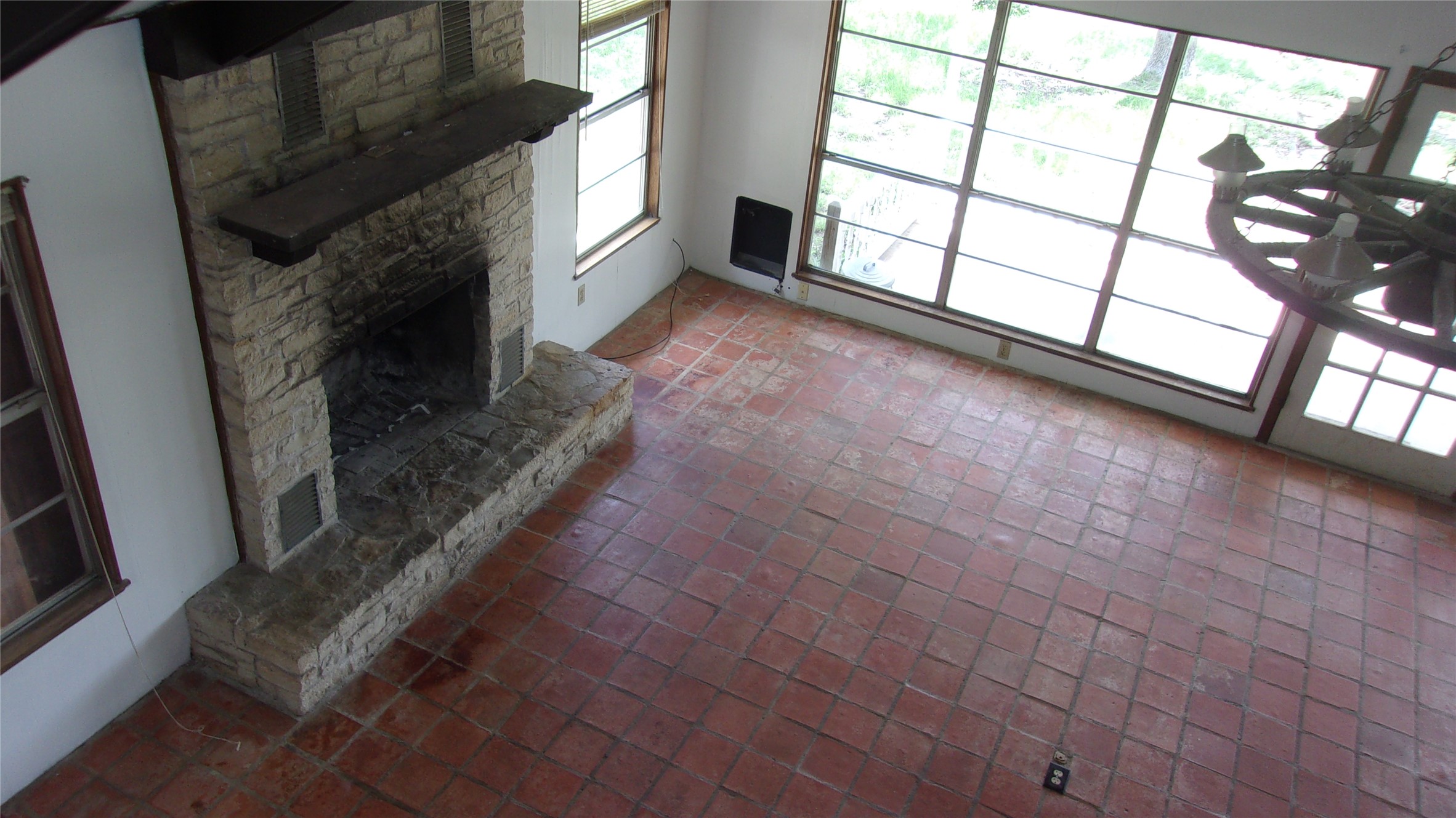 702 Cottonwood Creek Road Dripping Springs, TX 78620 - Photo 13 of 31 Spacious living area featuring a floor-to-ceiling stone fireplace with a substantial hearth, large grid-pane windows, terra cotta tile flooring, and a decorative ceiling light fixture