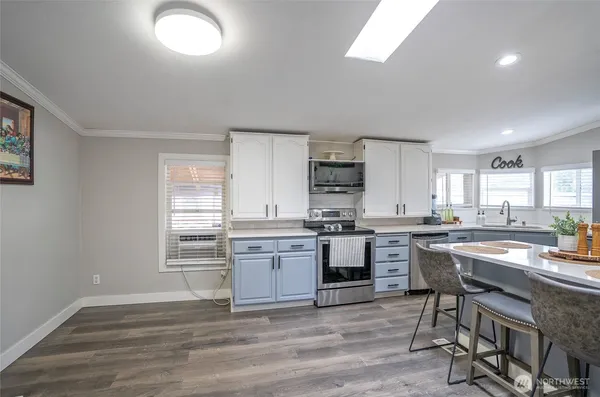 a kitchen with stainless steel appliances kitchen island granite countertop a stove top oven a sink dishwasher and white cabinets with wooden floor