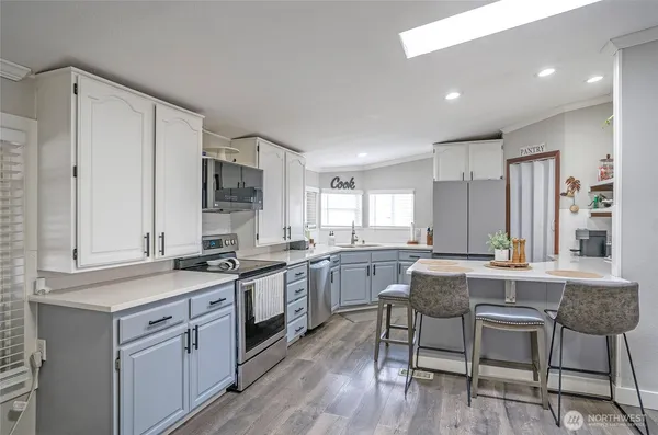 a kitchen with stainless steel appliances granite countertop a stove top oven a sink dishwasher and white cabinets with wooden floor