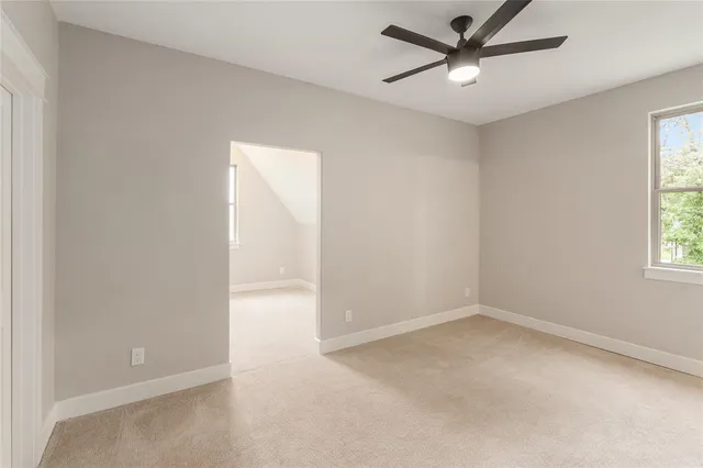 an empty room with chandelier fan and windows