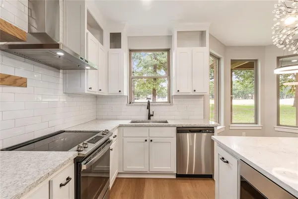 a large white kitchen with granite countertop a large counter top stainless steel appliances and cabinets
