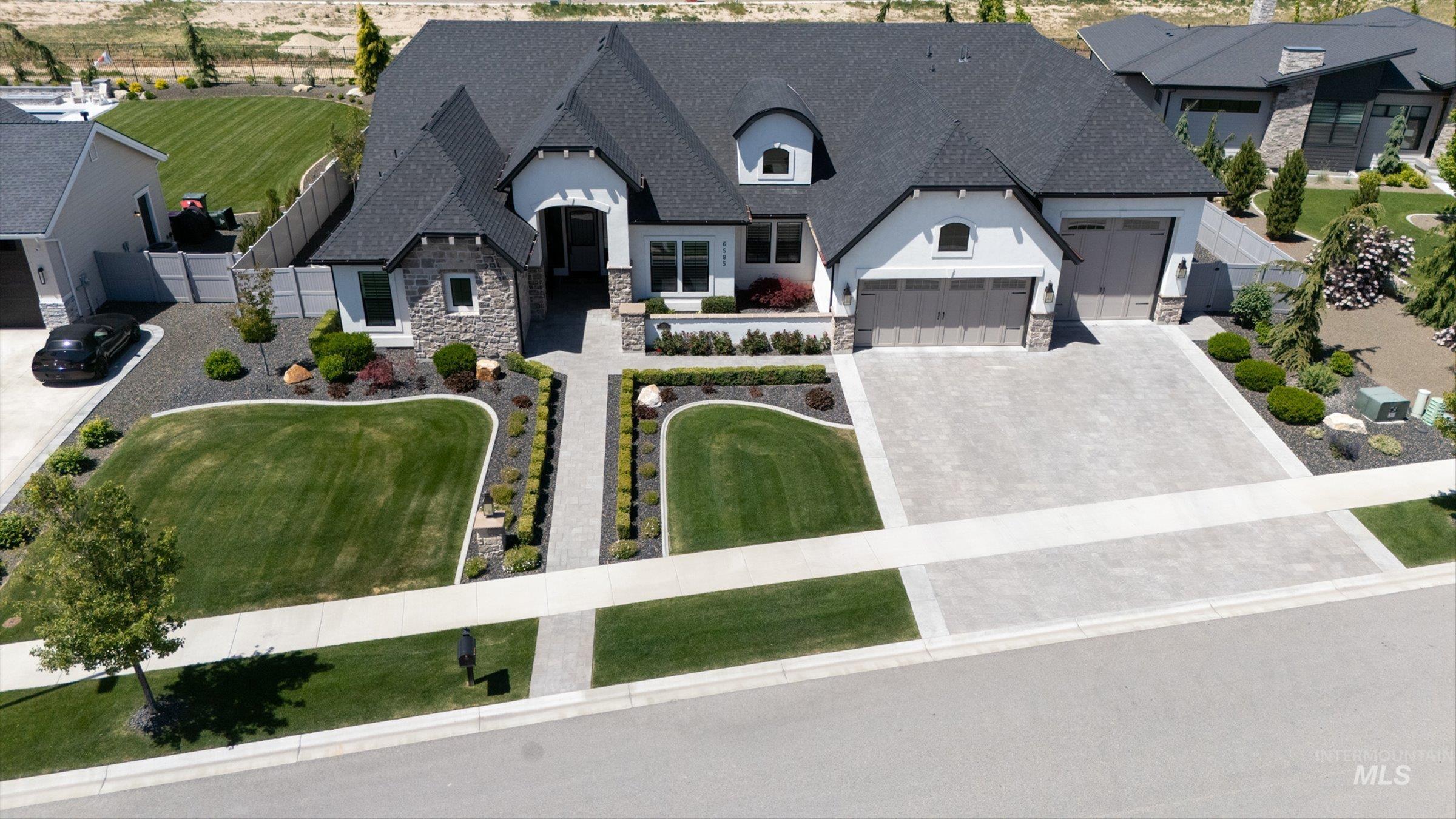 6585 South Pemberley Way Meridian, ID 83642 - Photo 43 of 43 Contemporary residence featuring an asphalt shingle roof, stone accents, two attached garages with neutral-toned doors, a concrete driveway, and a meticulously landscaped front yard with a paved walkway