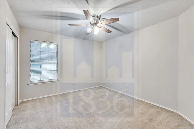 an empty room with chandelier fan and windows