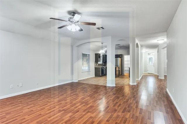 a view of an empty room and kitchen view with wooden floor