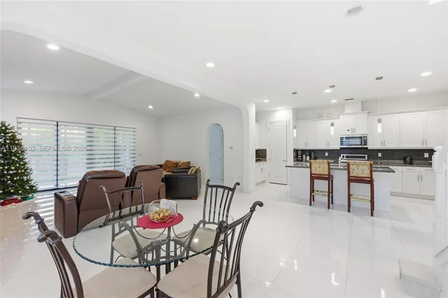 a kitchen with stainless steel appliances kitchen island granite countertop a dining table chairs and a refrigerator