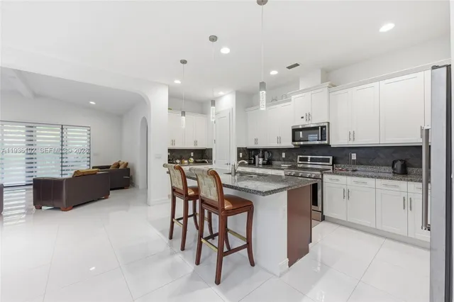 a kitchen with stainless steel appliances kitchen island granite countertop a stove a sink a refrigerator and white cabinets with wooden floor