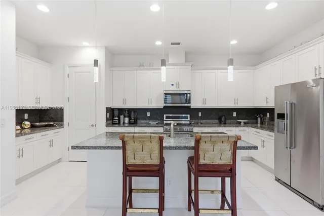 a kitchen with stainless steel appliances a stove a sink a refrigerator and white cabinets with wooden floor