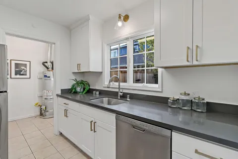 a kitchen with stainless steel appliances granite countertop a sink a window and white cabinets
