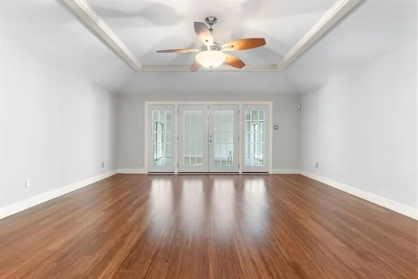 an empty room with wooden floor chandelier fan and windows