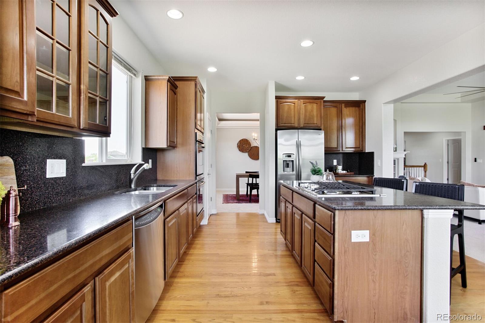 16283 Olive Way Brighton, CO 80602 - Photo 13 of 33 a kitchen with stainless steel appliances granite countertop a stove top oven a sink a refrigerator and white cabinets with wooden floor