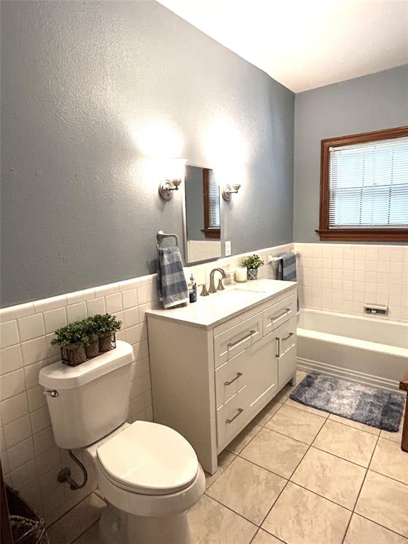 233 East High Street Wills Point, TX 75169 - Photo 17 of 35 Bathroom featuring a textured wall, vanity, tile walls, a wainscoted wall, and a bath