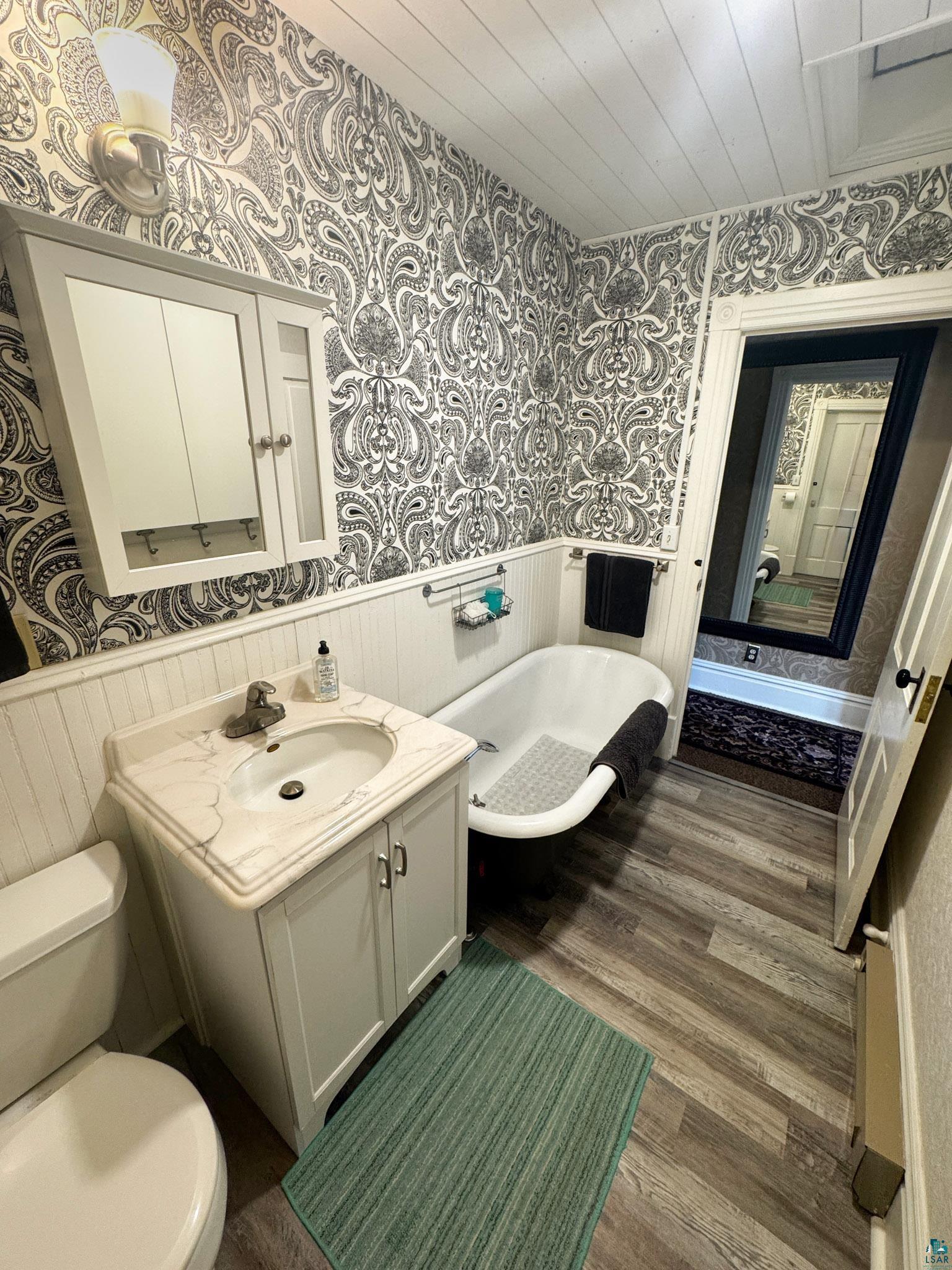 303 East 5th Street Washburn, WI 54891 - Photo 32 of 34 Bathroom featuring a classic clawfoot tub, wood-finish flooring, a white vanity with integrated sink, and patterned wallpaper
