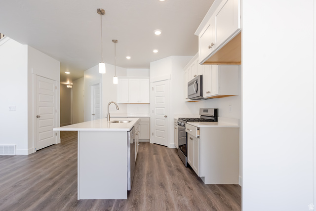5287 South Acacia Drive, Unit 714 Mapleton, UT 84664 - Photo 8 of 21 Kitchen featuring an island with an undermount sink and gooseneck faucet, white cabinetry, stainless steel range and microwave, wood-finish flooring, and recessed lighting