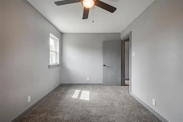 an empty room with chandelier fan and windows