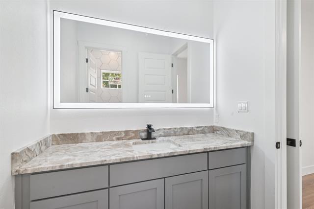 2936 Henry Road Lancaster, TX 75134 - Photo 24 of 28 Illuminated rectangular vanity mirror over a gray cabinet with a built-in sink, stone-finish countertop, and matte black faucet