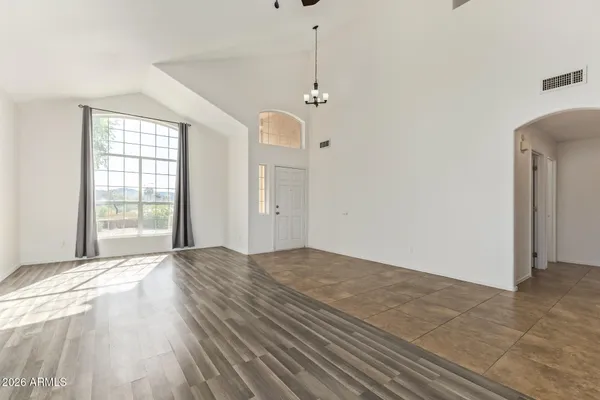 an empty room with wooden floor chandelier fan and windows