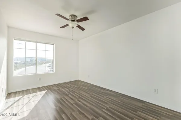 an empty room with wooden floor fan and windows