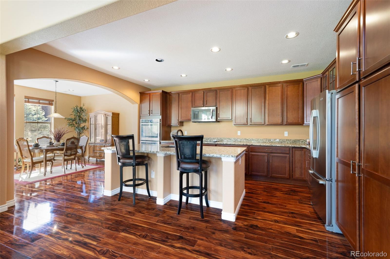 9472 Sori Lane Highlands Ranch, CO 80126 - Photo 4 of 43 a kitchen with stainless steel appliances granite countertop a refrigerator a stove top oven and a dining table with wooden floor