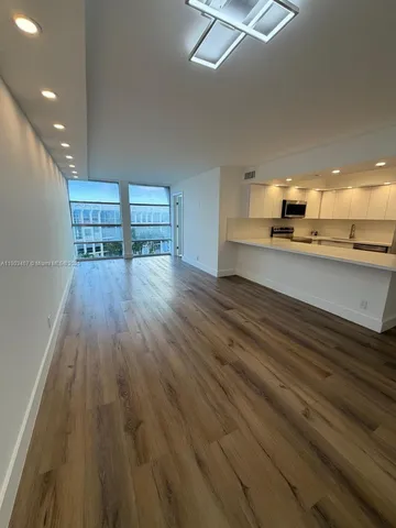 an empty room with wooden floor kitchen view and windows