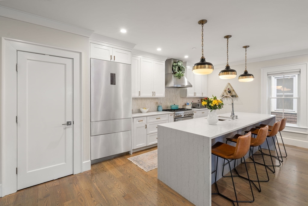 654 East 7th Street, Unit 3 Boston, MA 02127 - Photo 4 of 28 a kitchen with stainless steel appliances granite countertop a sink a refrigerator a stove a dining table and chairs with wooden floor