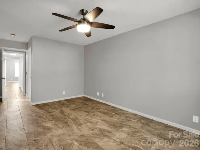 an empty room with a chandelier fan and windows