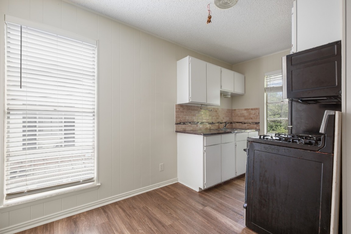 5300 Guadalupe Street, Unit 6202 Austin, TX 78751 - Photo 2 of 10 Kitchen with a textured ceiling, range with gas stovetop, decorative backsplash, white cabinets, and wood finished floors
