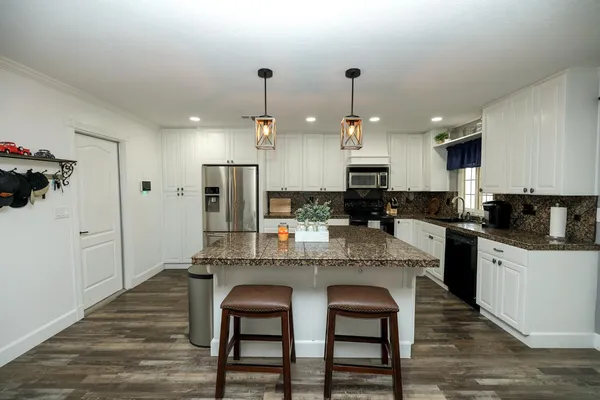 a kitchen with stainless steel appliances granite countertop a sink a stove a refrigerator and island with wooden floor
