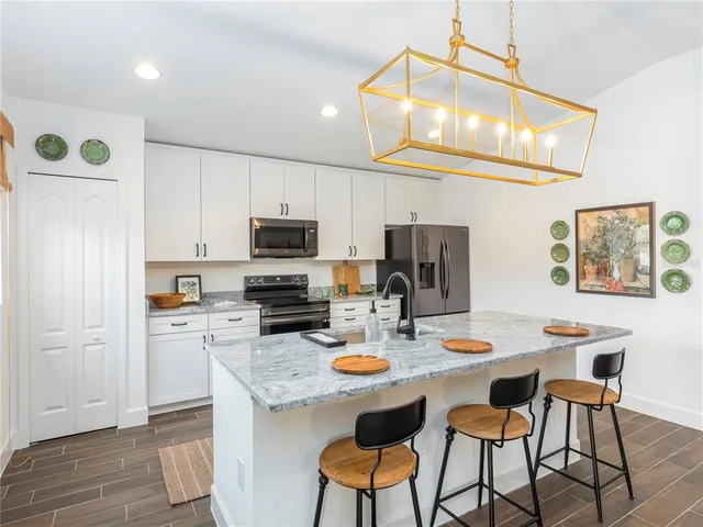 a kitchen with stainless steel appliances granite countertop a stove a refrigerator a sink a dining table and chairs with wooden floor