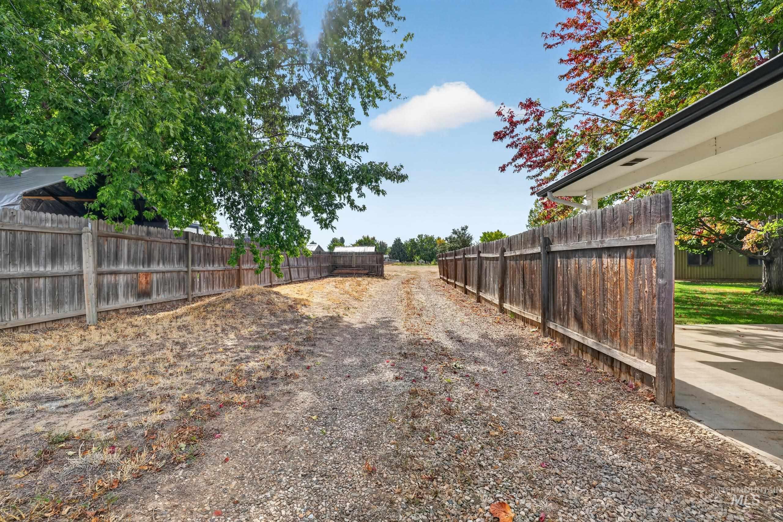 9055 West Highlander Road Boise, ID 83709 - Photo 34 of 39 Gravel driveway with wood fencing, mature trees, and a covered carport