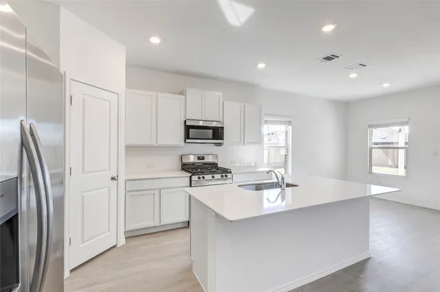 a kitchen with stainless steel appliances a sink a stove a refrigerator cabinets and a window