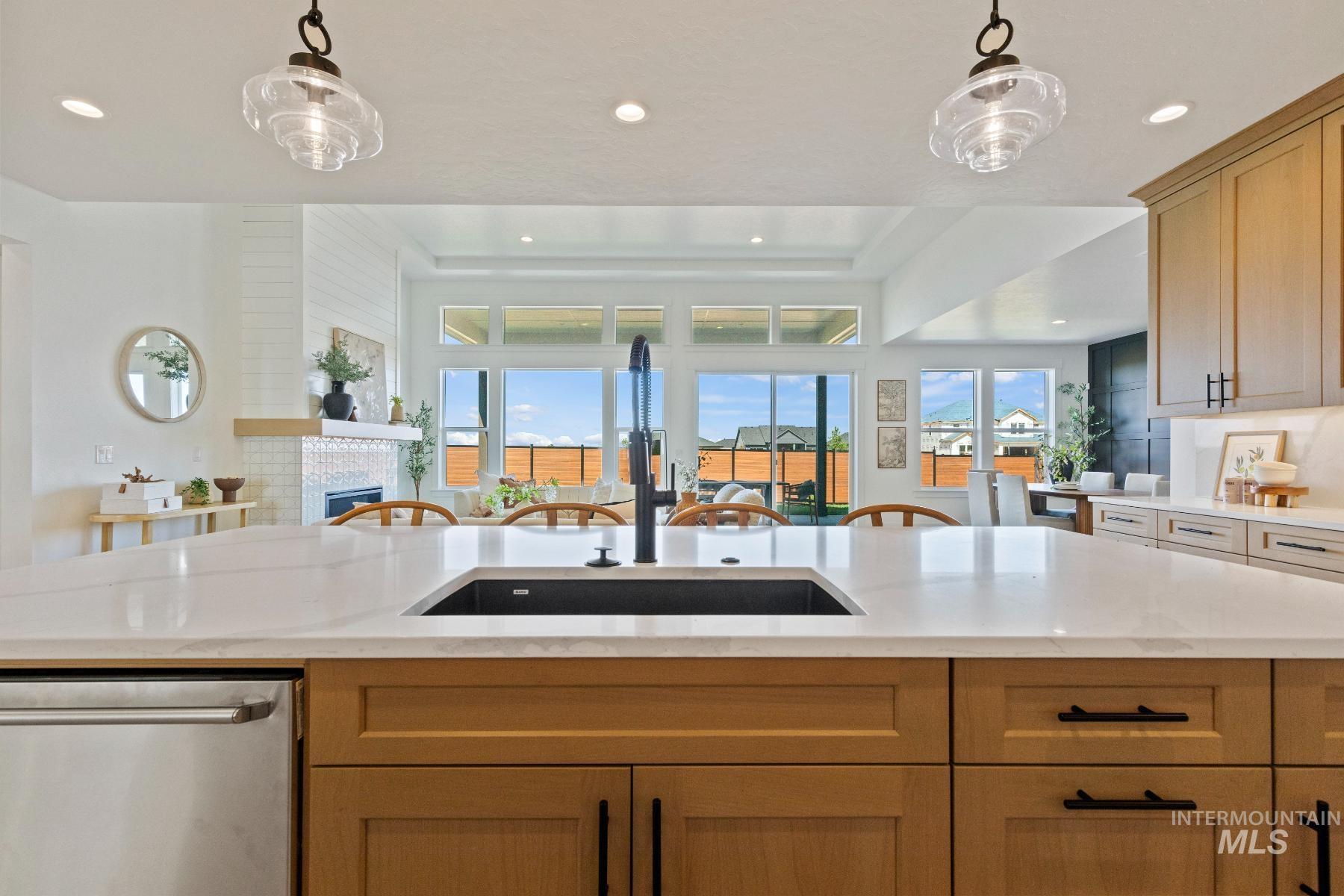 8650 West Inspirado Street Meridian, ID 83646 - Photo 29 of 30 Kitchen with stainless steel dishwasher, light stone counters, pendant lighting, open floor plan, and a glass covered fireplace