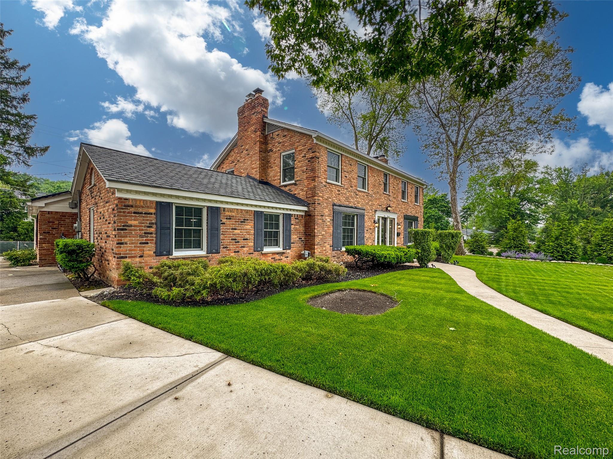 View of front of house with a front lawn, a chimney, brick siding, and a shingled roof