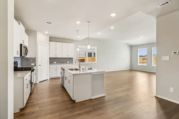 a kitchen with stainless steel appliances granite countertop a stove top oven a sink dishwasher a refrigerator and white cabinets with wooden floor