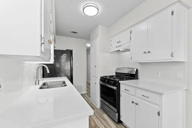 a kitchen with granite countertop a sink dishwasher stove and white cabinets with wooden floor