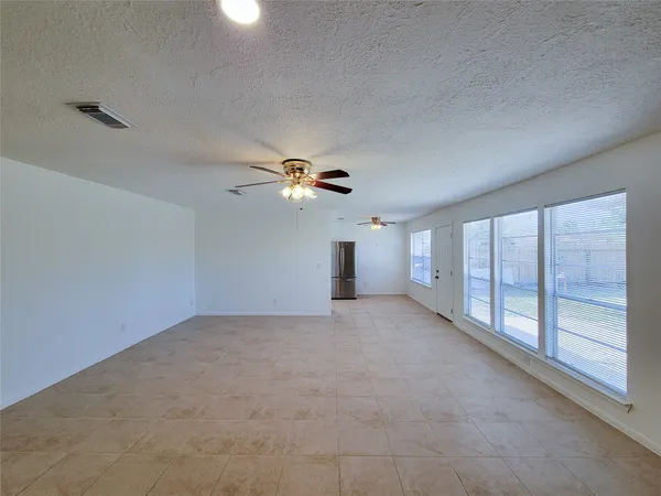 an empty room with chandelier fan and windows