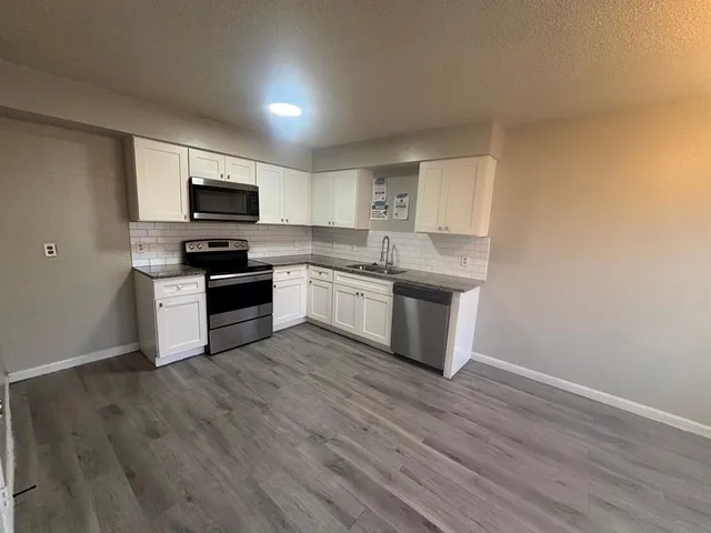 a kitchen with stainless steel appliances granite countertop a stove top oven a sink a refrigerator white cabinets and wooden floor