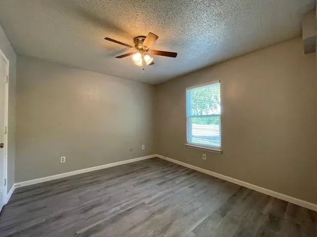 an empty room with wooden floor fan and windows