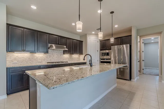a large kitchen with kitchen island a large counter top stainless steel appliances and cabinets