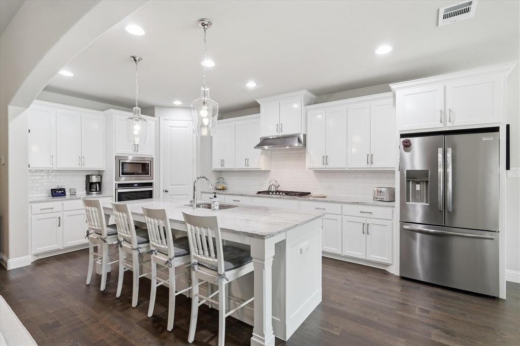 9708 Surveyor Road Oak Point, TX 75068 - Photo 5 of 34 Gourmet kitchen featuring a large central island with seating, white shaker-style cabinetry, stainless steel appliances, and wood-finish flooring