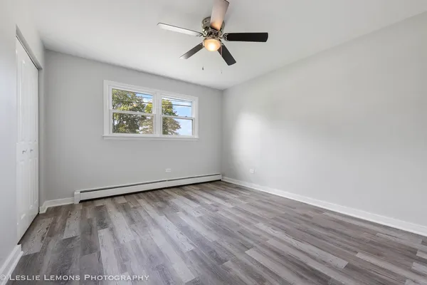 an empty room with wooden floor chandelier fan and windows